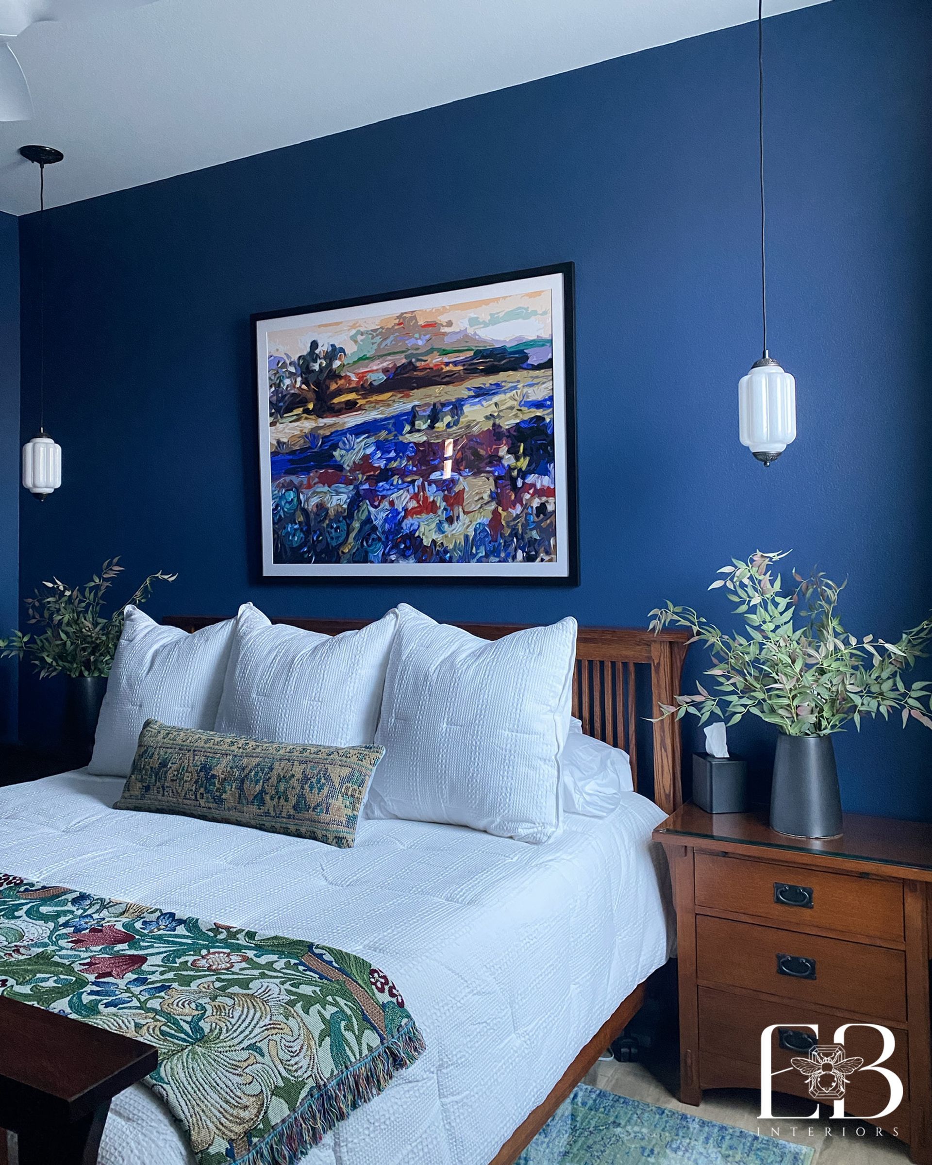 Bedroom with blue walls, wood bed, white bedding, landscape art, hanging lights, and nightstand.