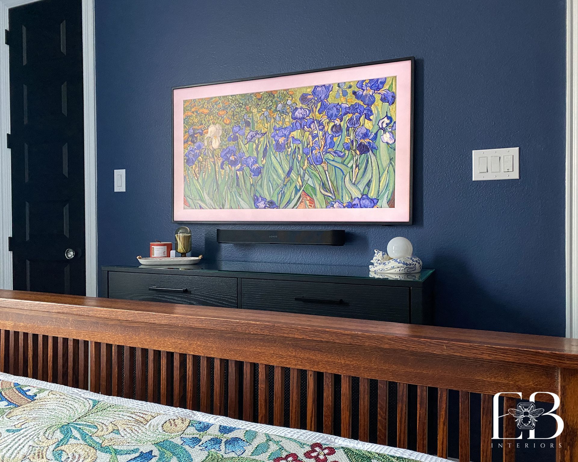 Bedroom with a blue wall, black door, and a TV displaying a floral painting above a black cabinet.