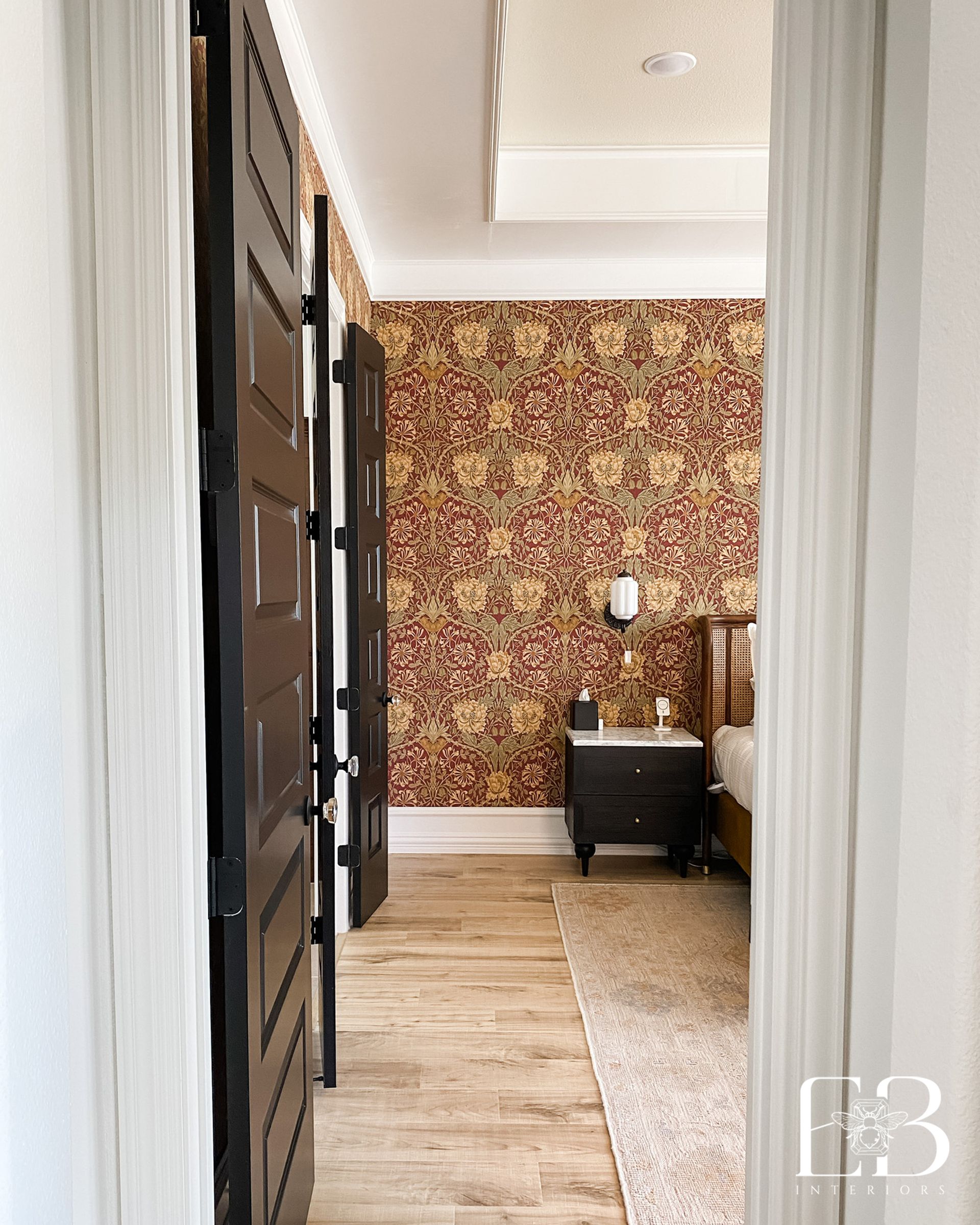 Dark doorway leads to a bedroom with patterned red wallpaper, wood floor, and a nightstand.