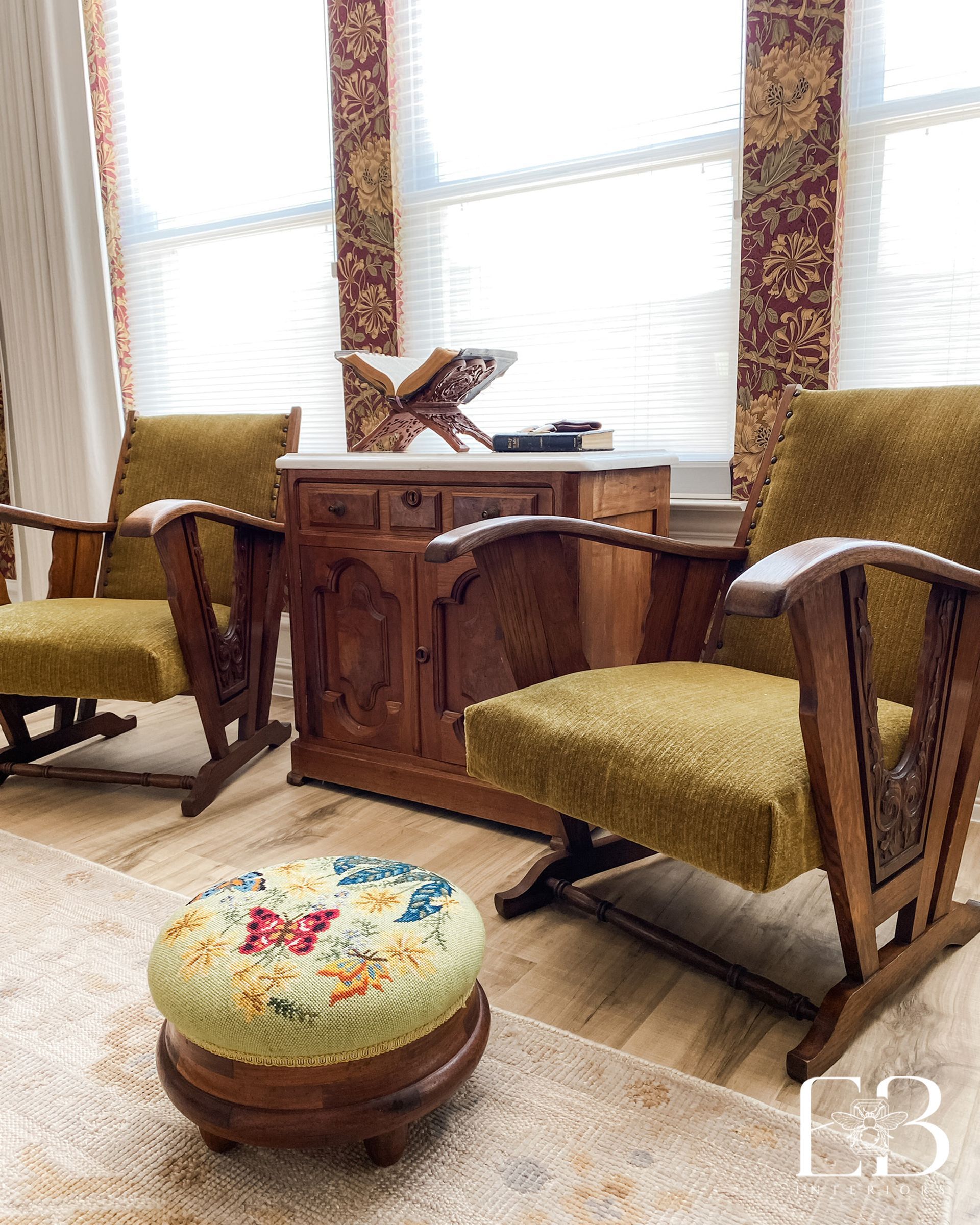 Cozy living room with two wooden armchairs, small cabinet, and a floral ottoman.