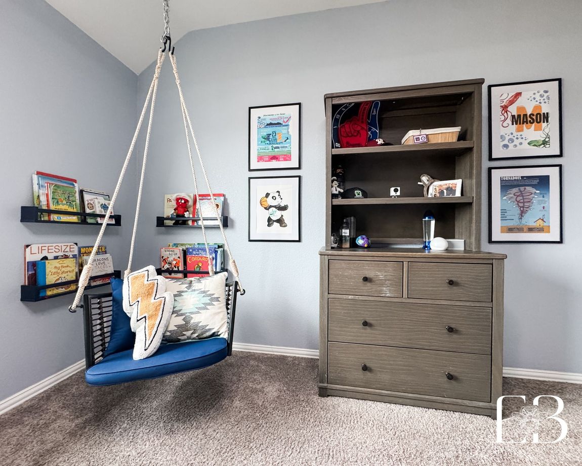Children’s reading nook with blue hanging chair, framed art, and floating bookshelves by Emerald Bee Interiors.