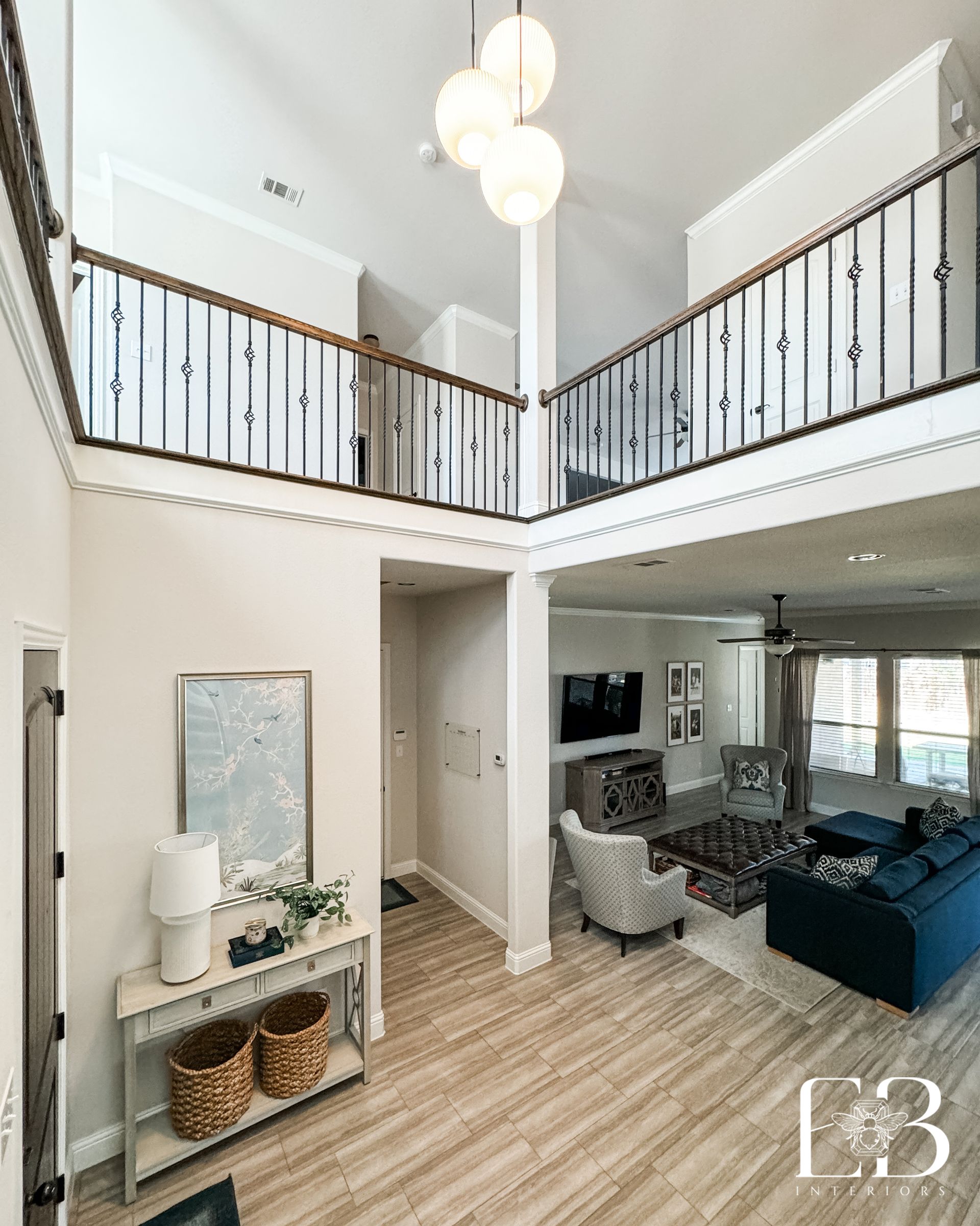 Two-story living room with balcony railing, wood accents, and layered neutrals designed by Emerald Bee Interiors.
