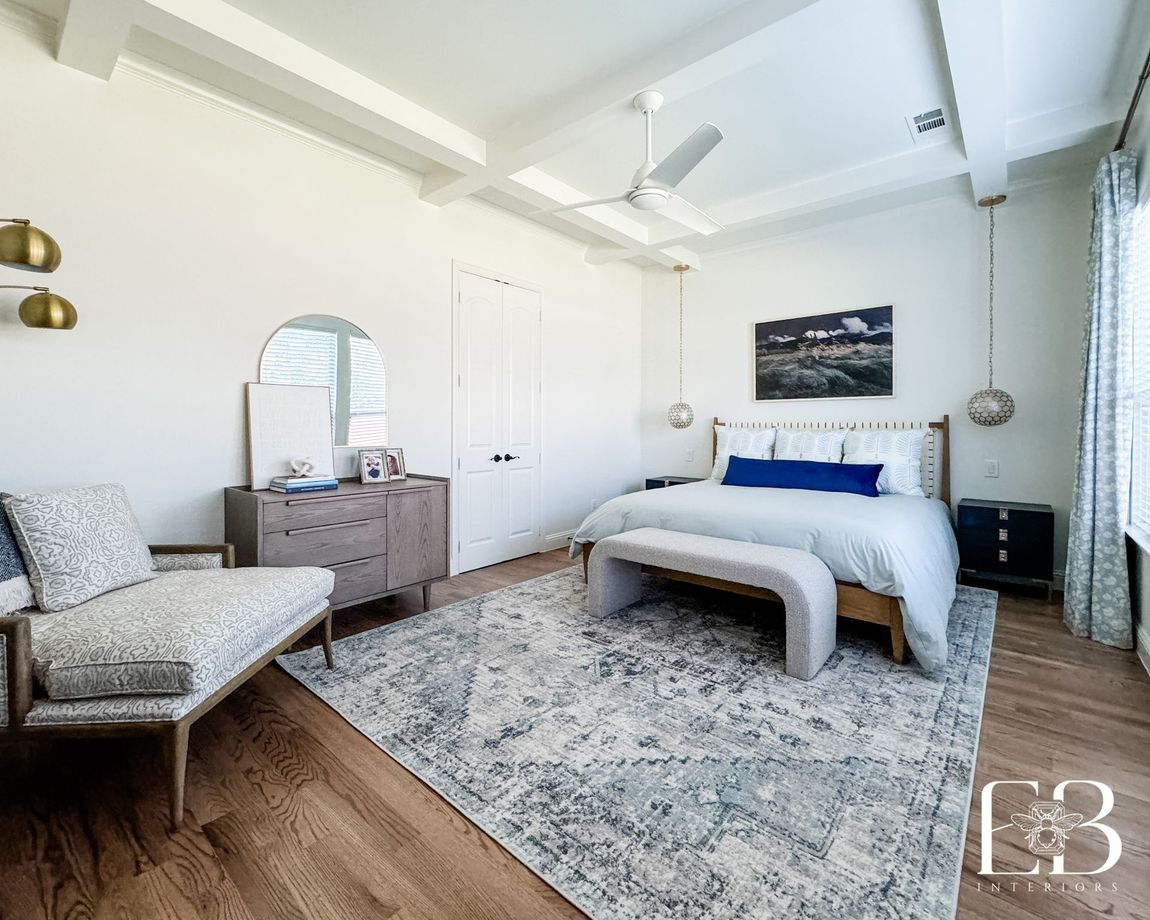 Primary bedroom by Emerald Bee Interiors with coffered ceiling, woven bed, and soft blue accents for a serene coastal feel.