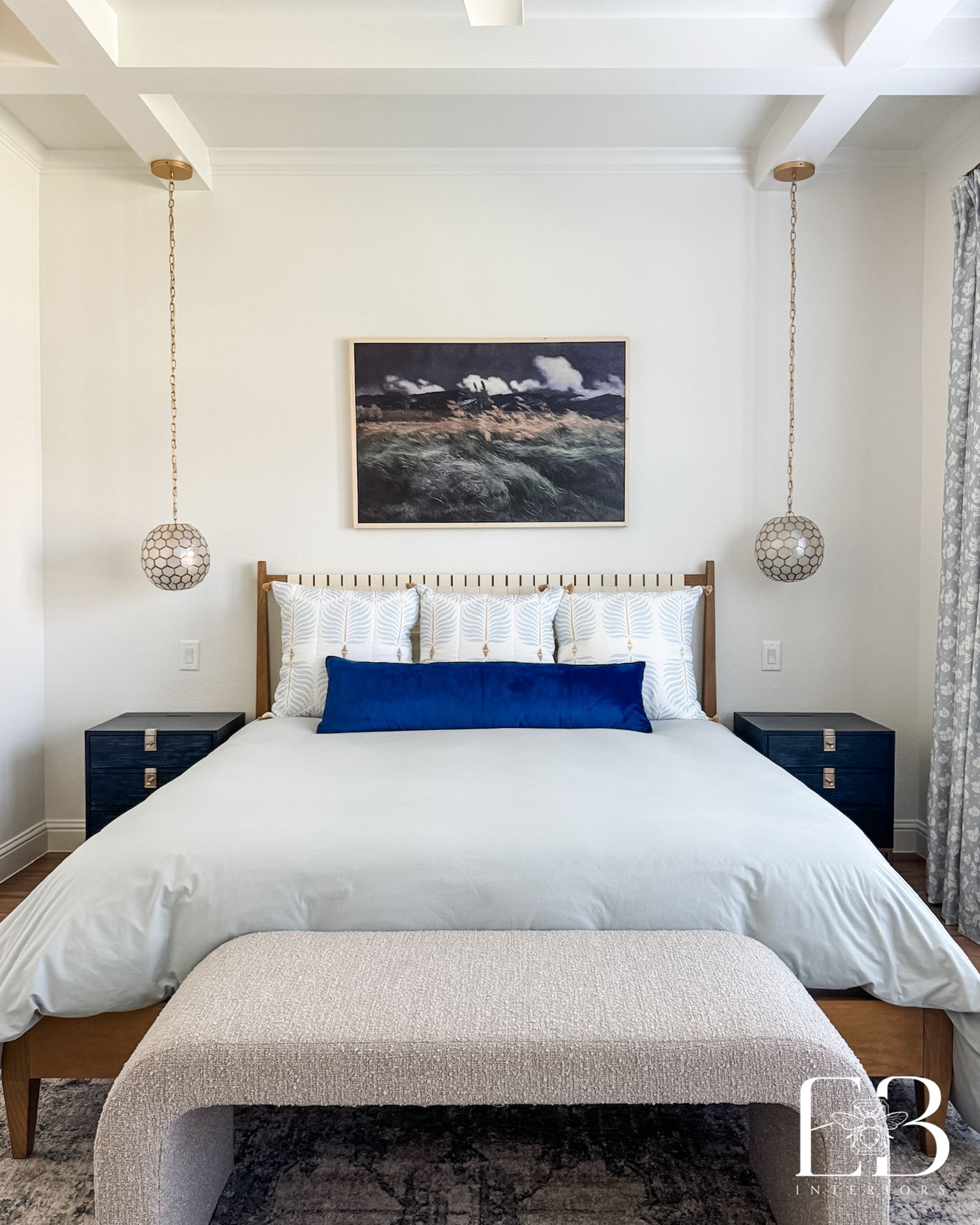 Primary bed with coastal palette, navy velvet bolster, and geometric pendants designed by Emerald Bee Interiors.