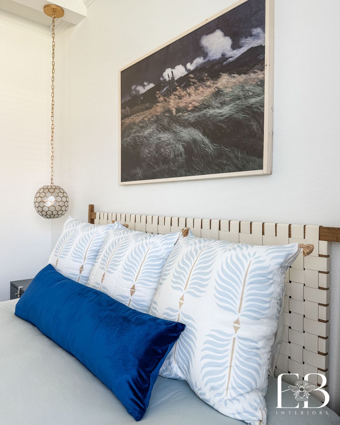 Bed styling with woven headboard, patterned pillows, and bold blue velvet lumbar designed by Emerald Bee Interiors.