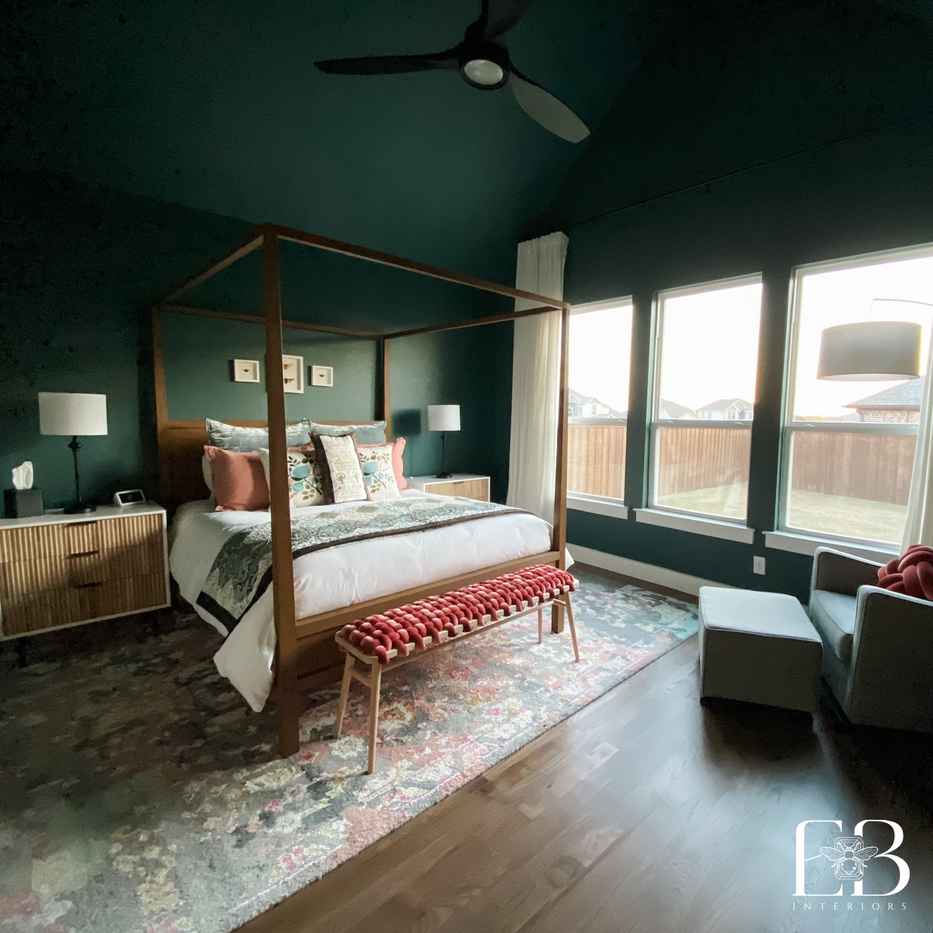 Cozy bedroom with green walls, four-poster bed, rug, bench, and large windows with natural light.