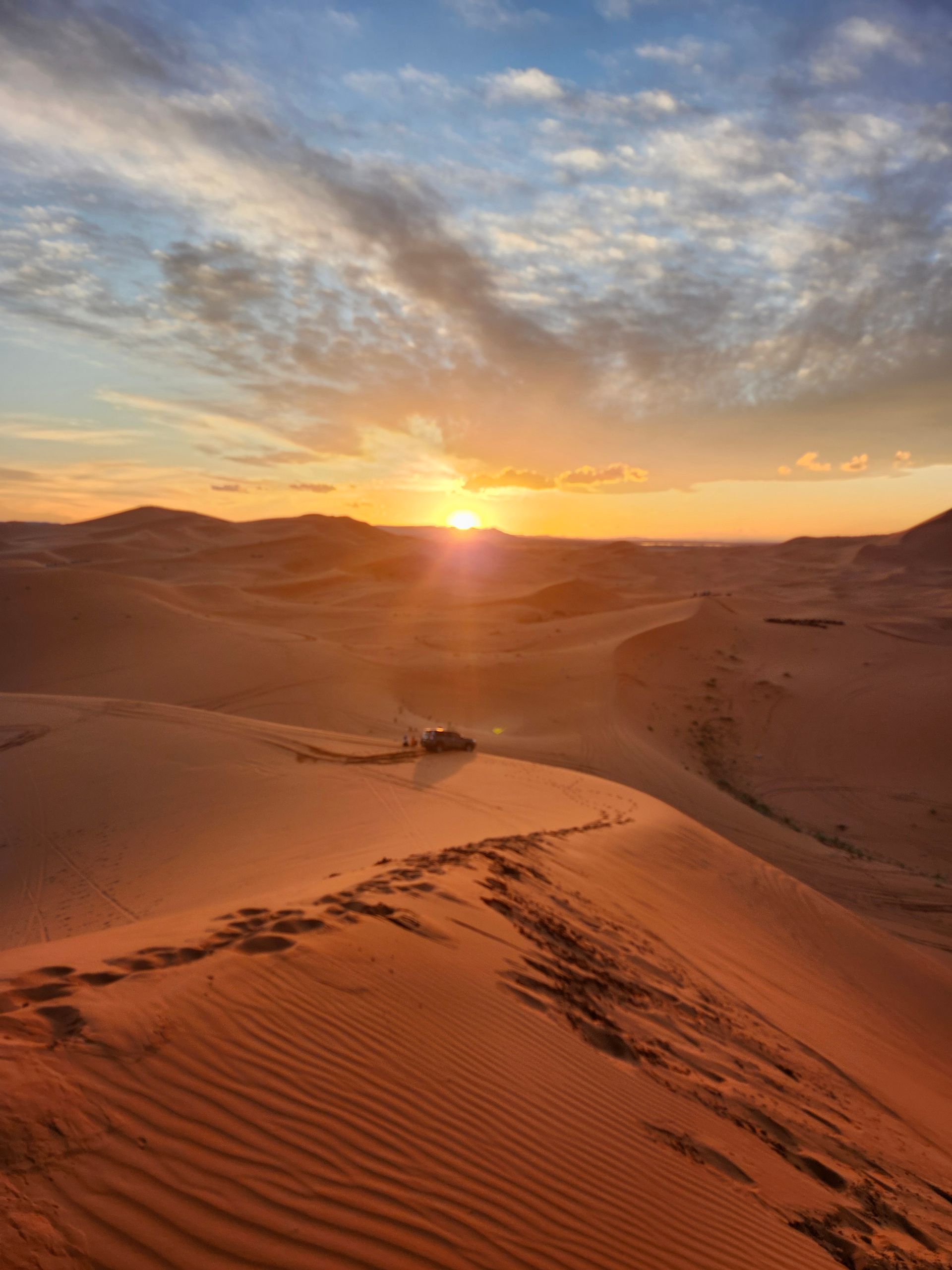 The sun is setting over a desert landscape with sand dunes.