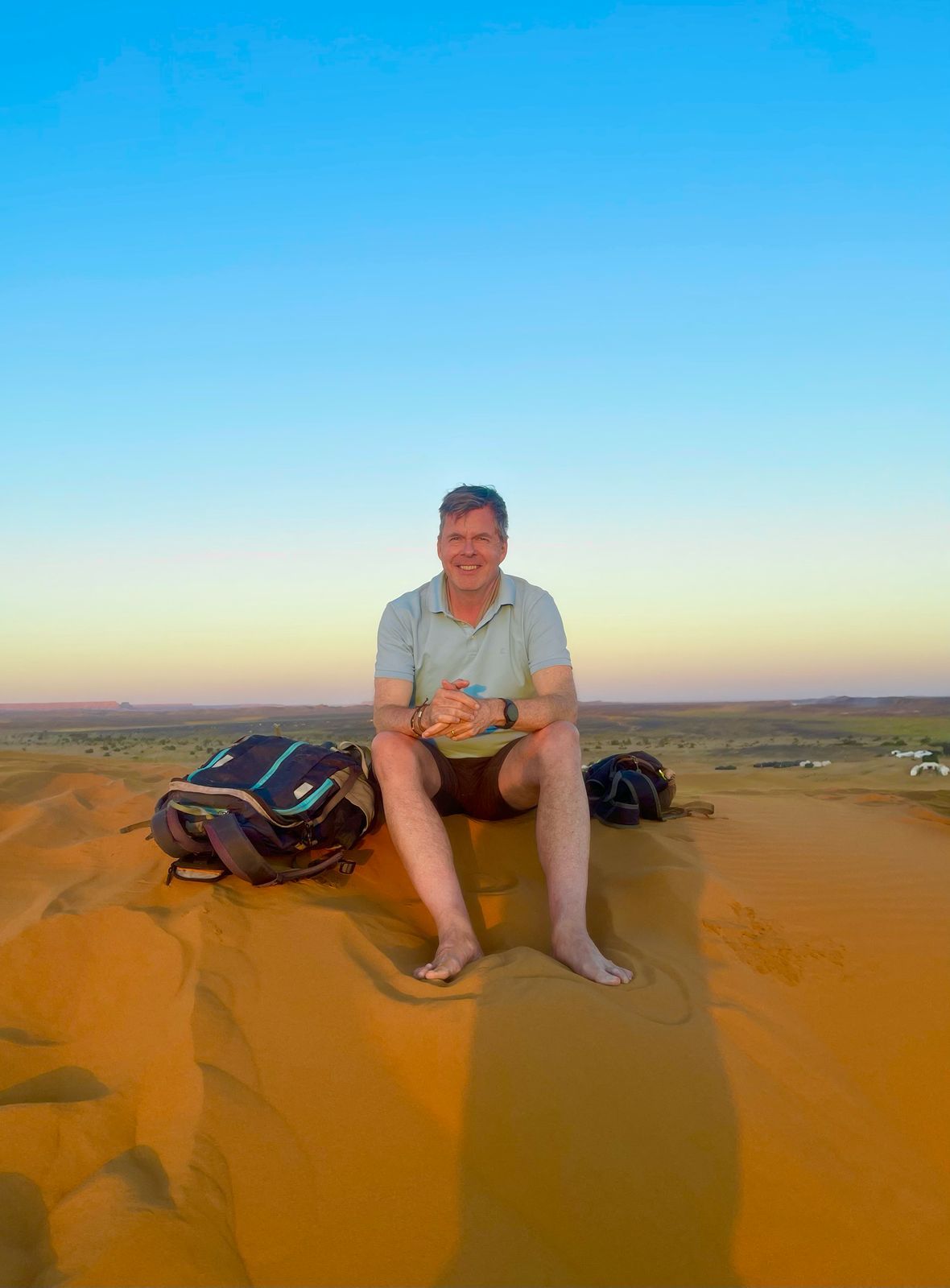 A man is sitting on top of a sand dune in the desert.
