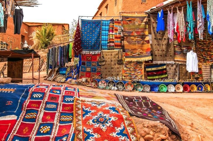 A row of colorful rugs are sitting in front of a building.
