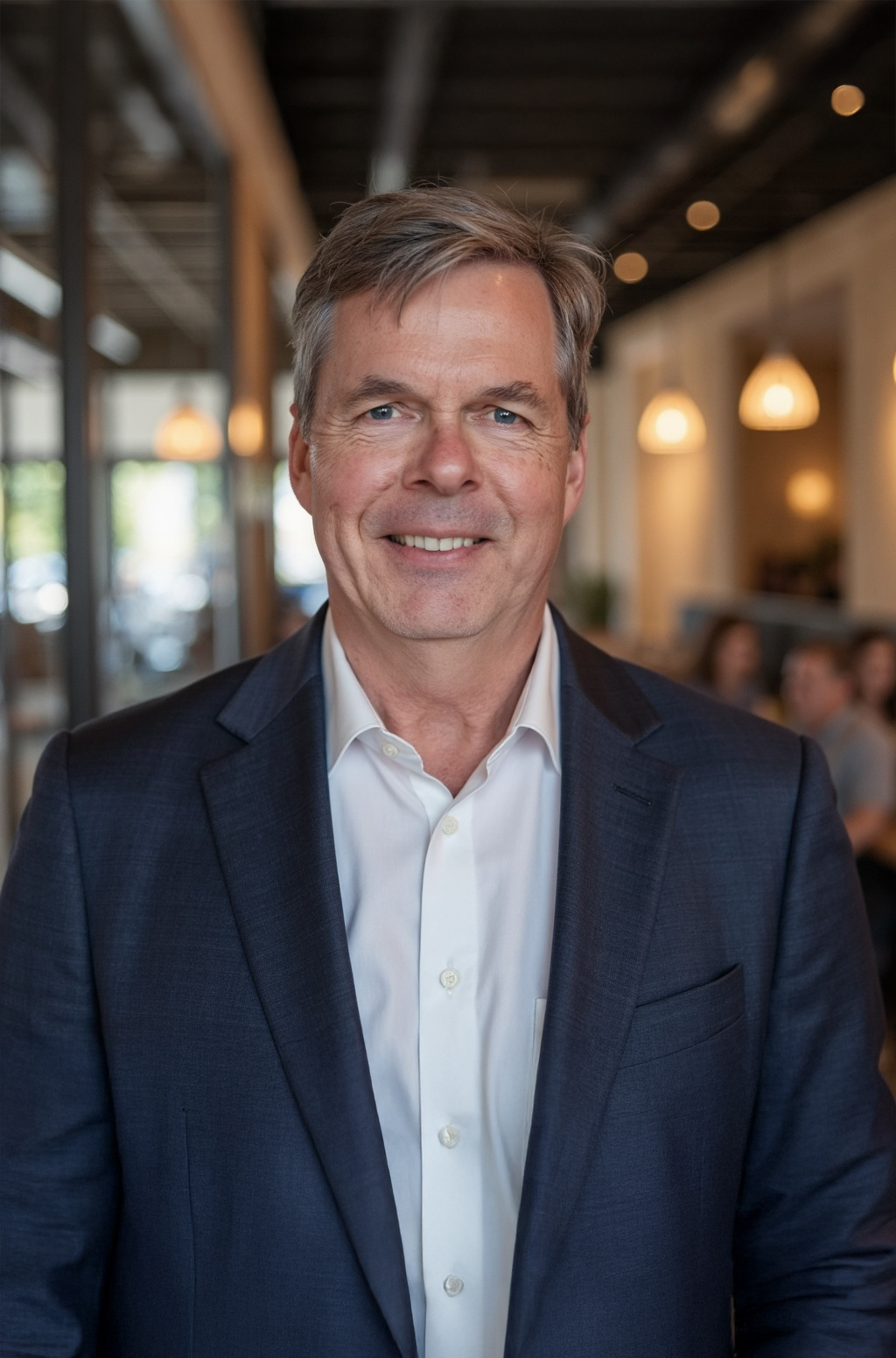 Man in a dark blue blazer and white shirt smiles; soft-lit background.