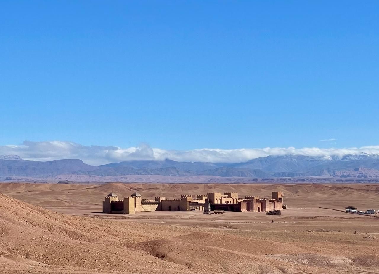 A desert landscape with mountains in the background and a building in the foreground