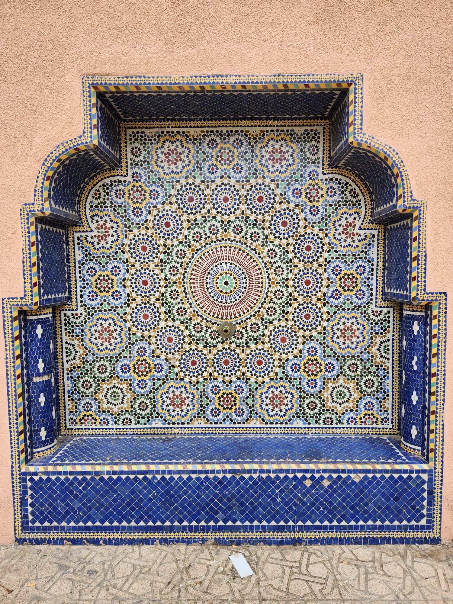 A colorful mosaic on a wall with a fountain in the background.