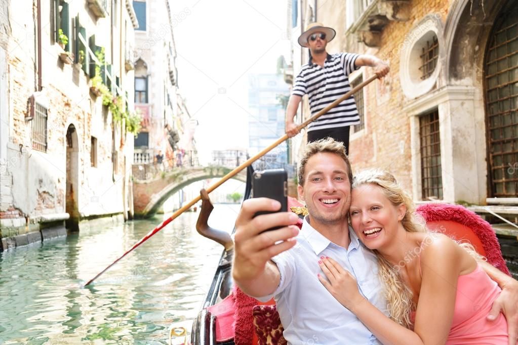 Couple taking a selfie on a gondola in Venice with the gondolier in the background.