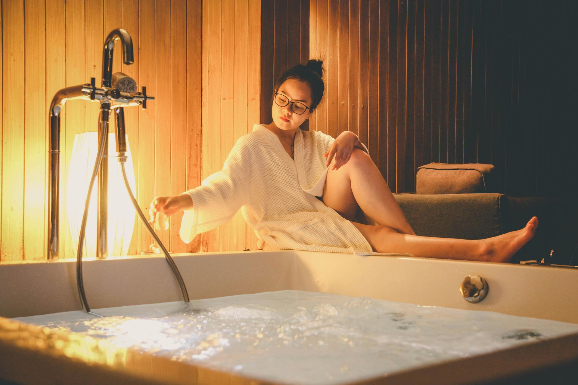 A woman in a bathrobe is sitting in a jacuzzi tub.