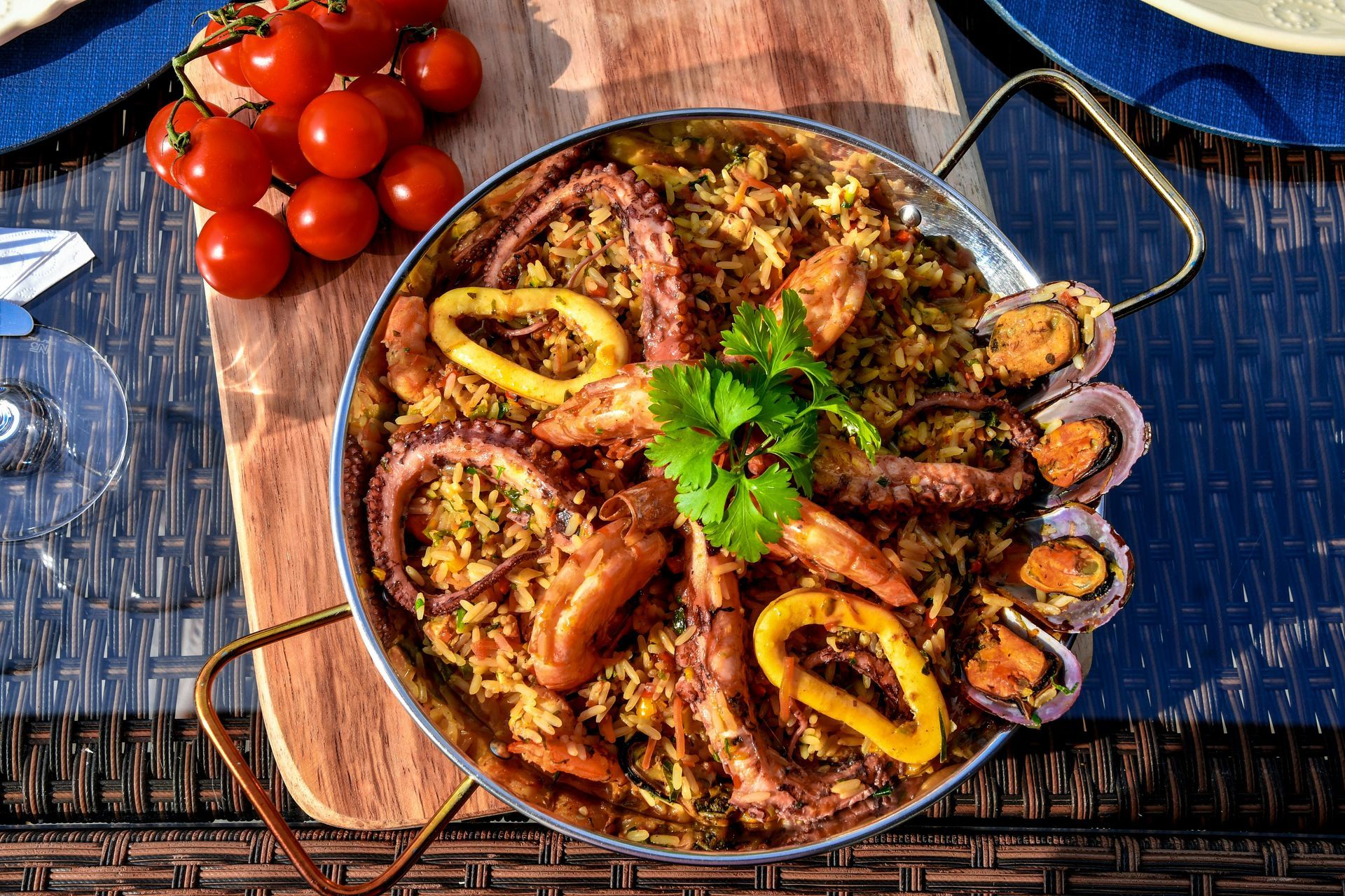 Seafood paella in metal pan with octopus, squid, mussels, rice, tomatoes, on wooden board.