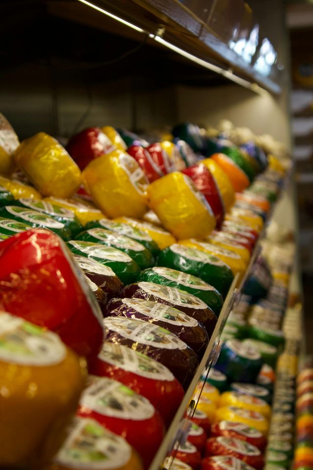 Cheeses in colorful wax coatings displayed on shelves.