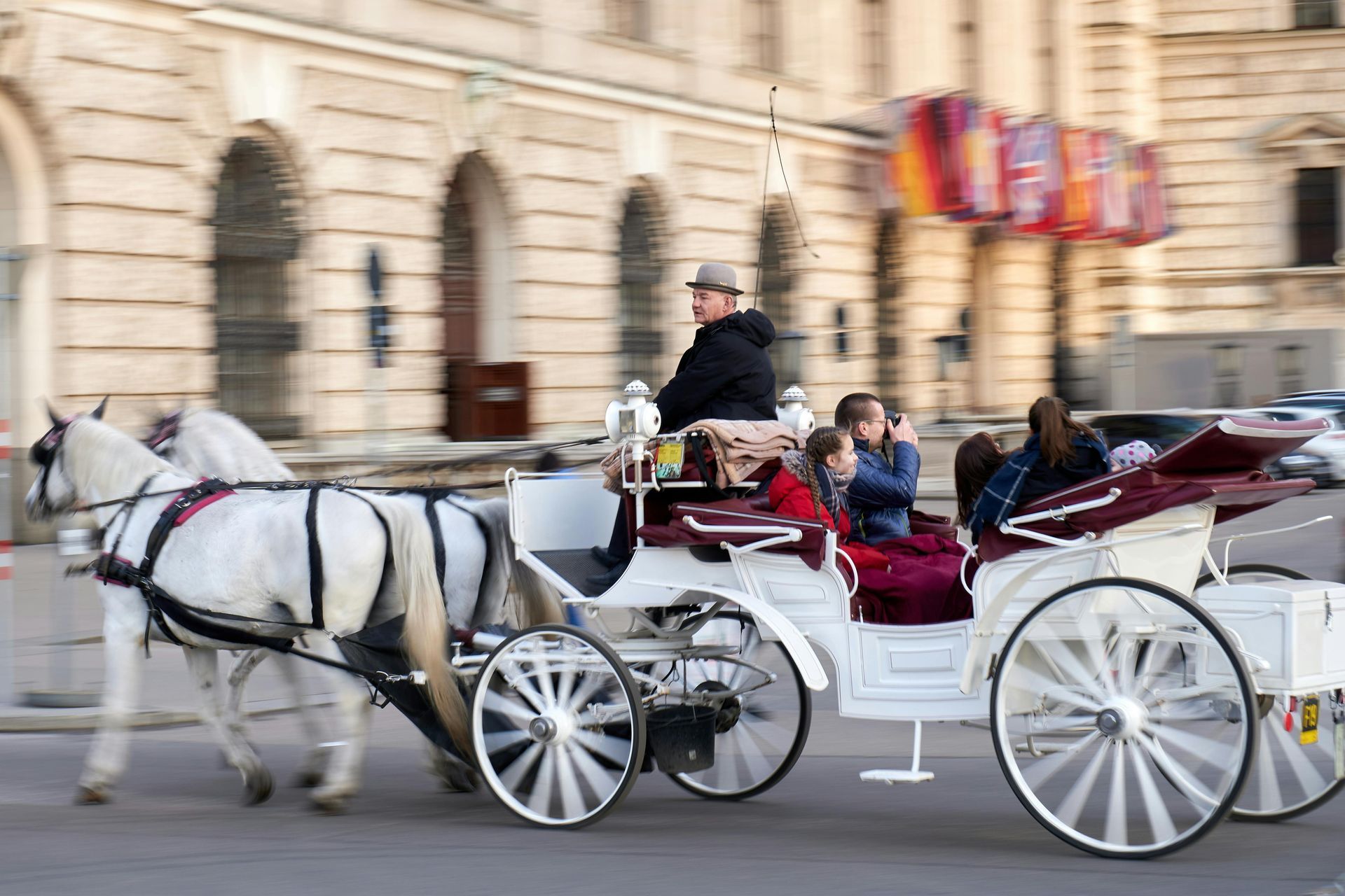 A horse drawn carriage is driving down a city street. Vienna. Fiaker.