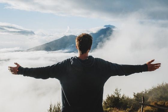 A man is standing on top of a mountain with his arms outstretched.