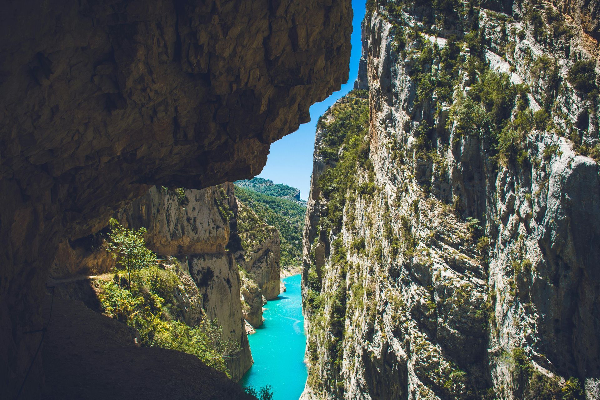 Narrow gorge with turquoise water, tall rock walls, and blue sky.