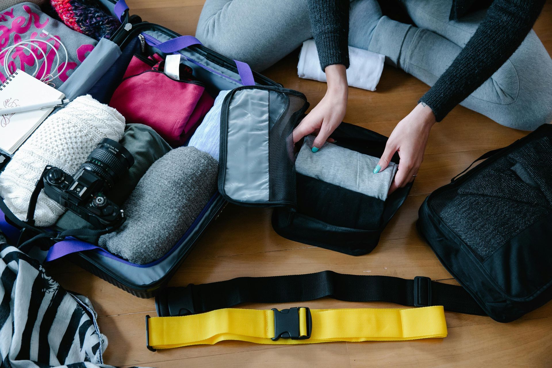 A woman is sitting on the floor packing a suitcase.