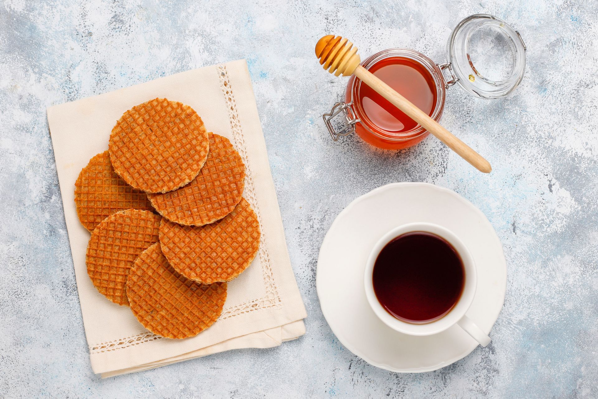 Stroopwafels on a napkin, with a cup of tea and a jar of honey.