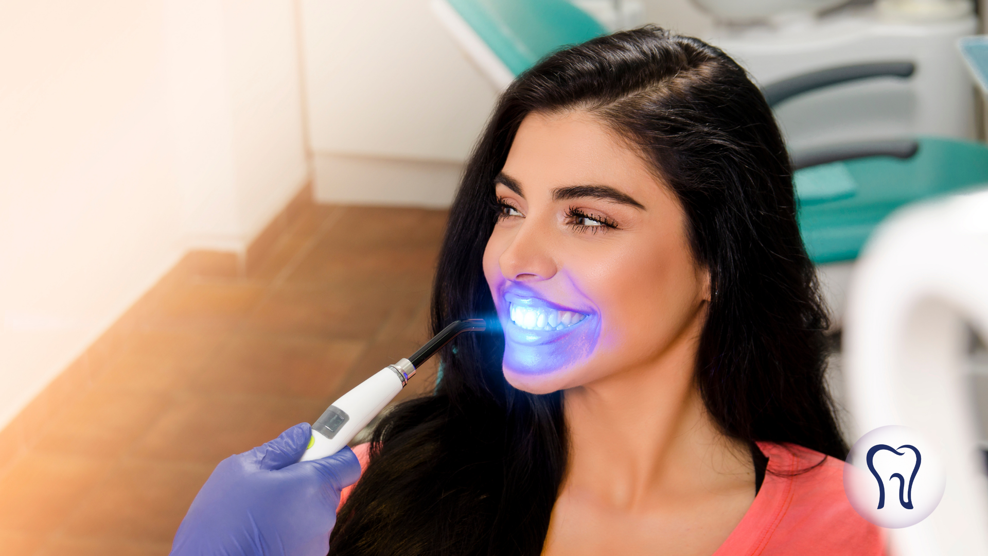 Woman receiving teeth whitening treatment with blue light in a dental office.