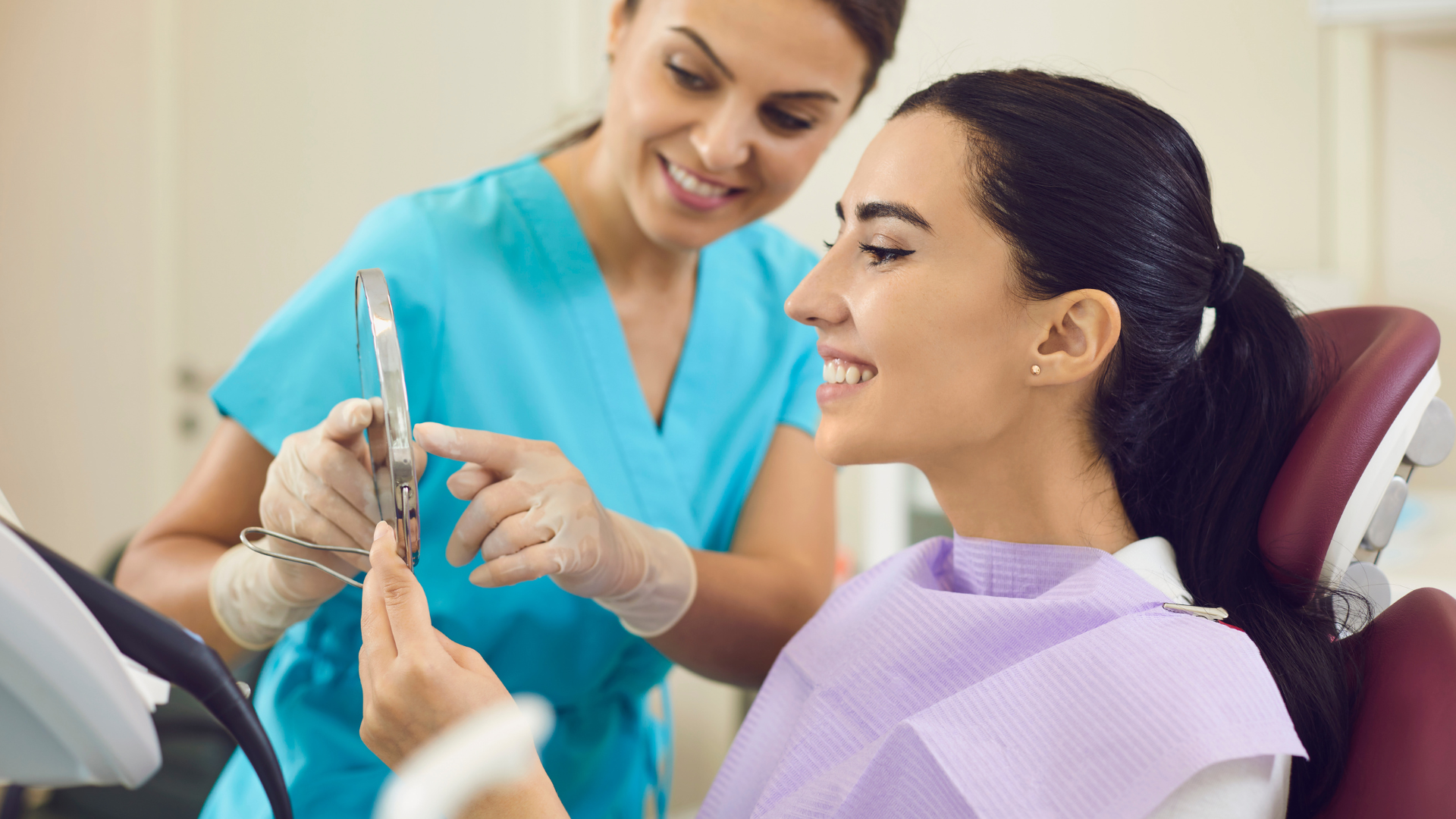 A woman is sitting in a dental chair while a dentist examines her teeth.