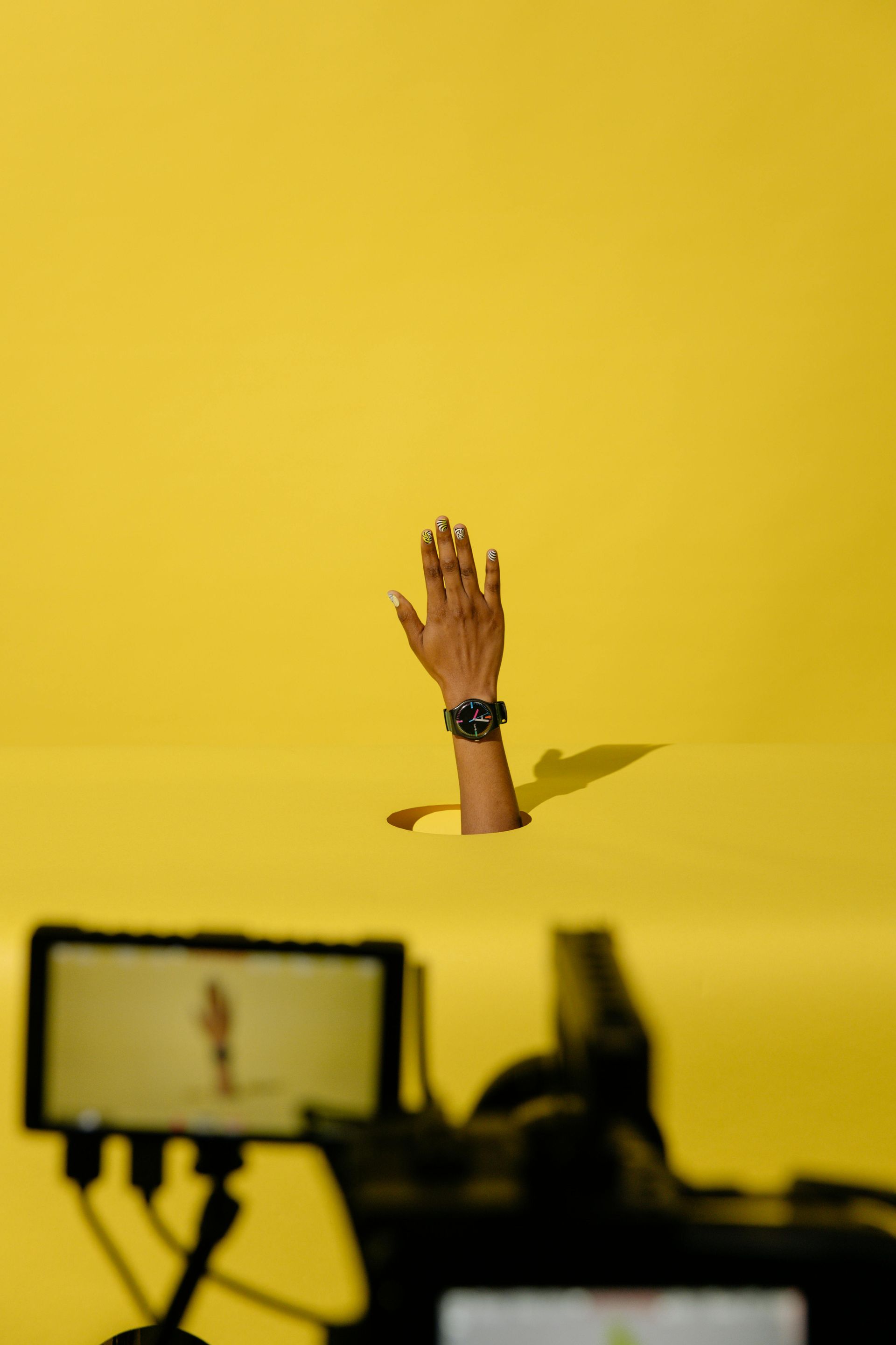 A hand wearing a watch is flying through the air in front of a yellow background.