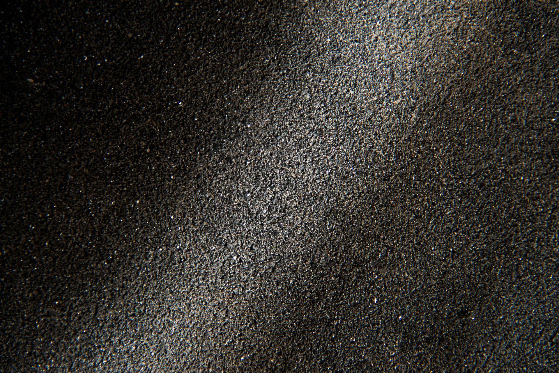 Black sand with hints of gray and light reflecting off the grains.