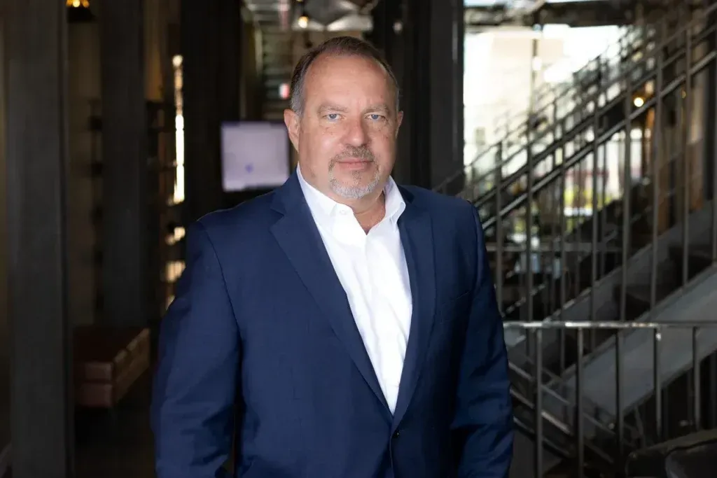 A man in a suit and white shirt is standing in front of stairs.