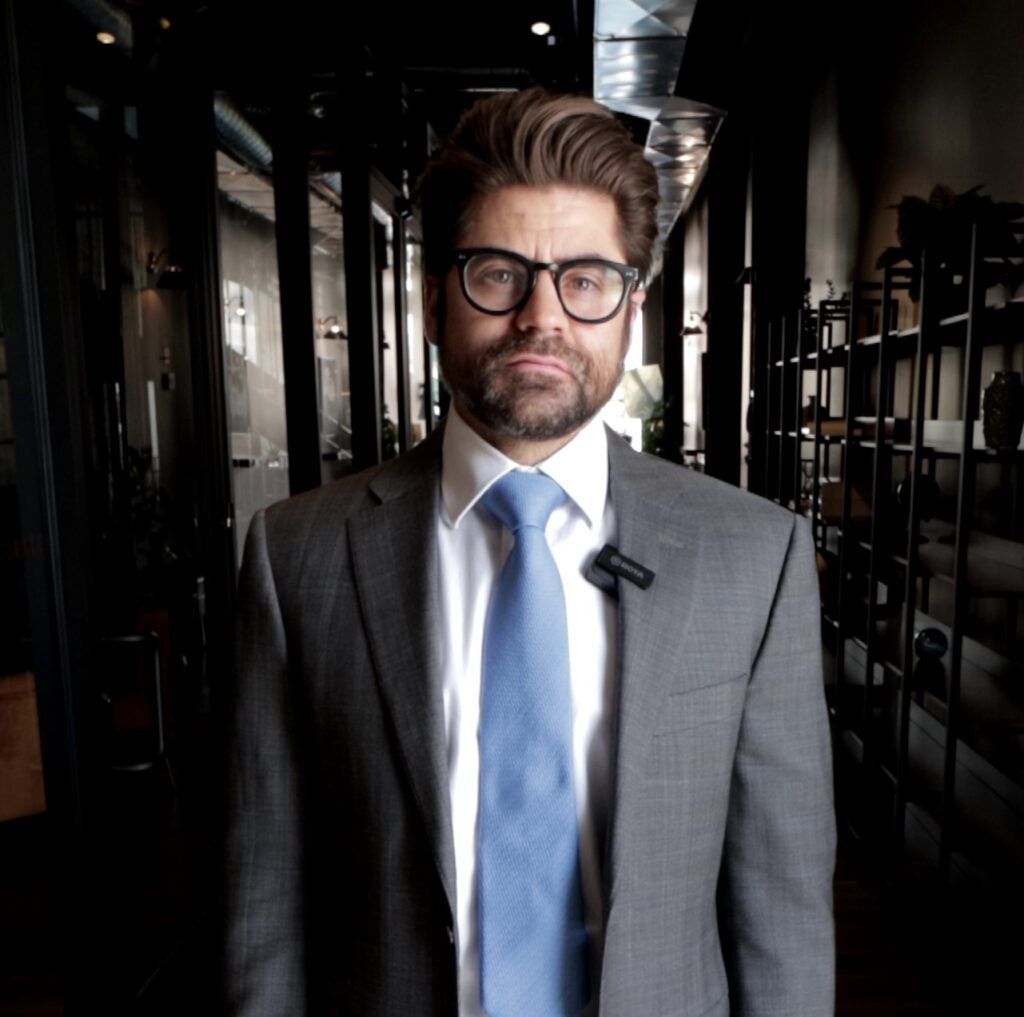 A man in a suit and tie stands in a dark hallway