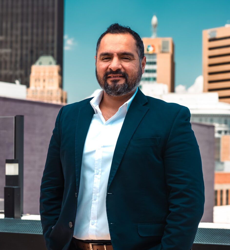 A man in a suit and white shirt is standing in front of a city skyline.