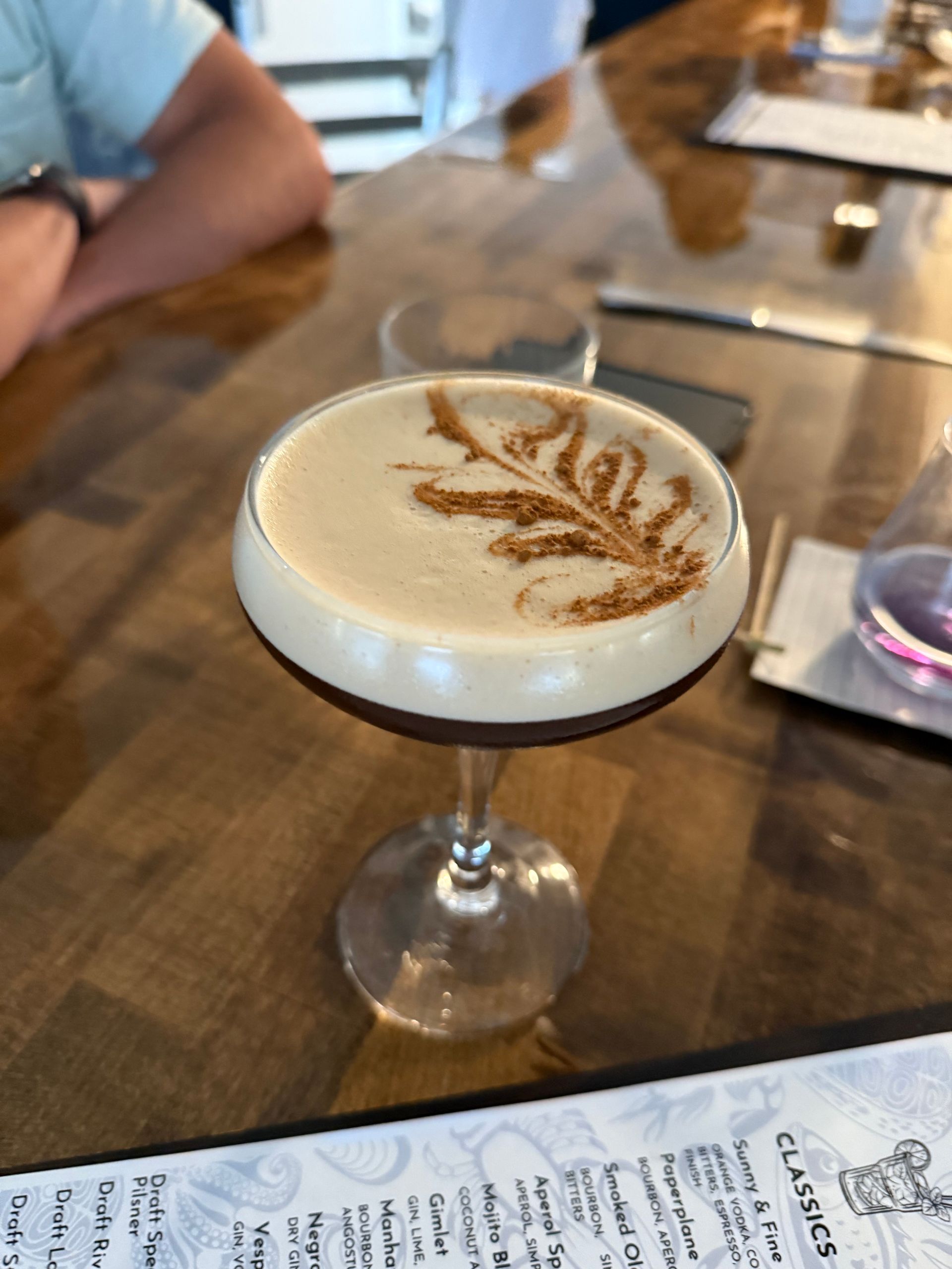 A martini with a leaf on the top is on a table next to a menu