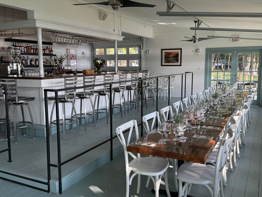 A restaurant with a long table and chairs and a bar.