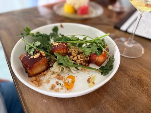A bowl of food on a wooden table next to a glass of wine.
