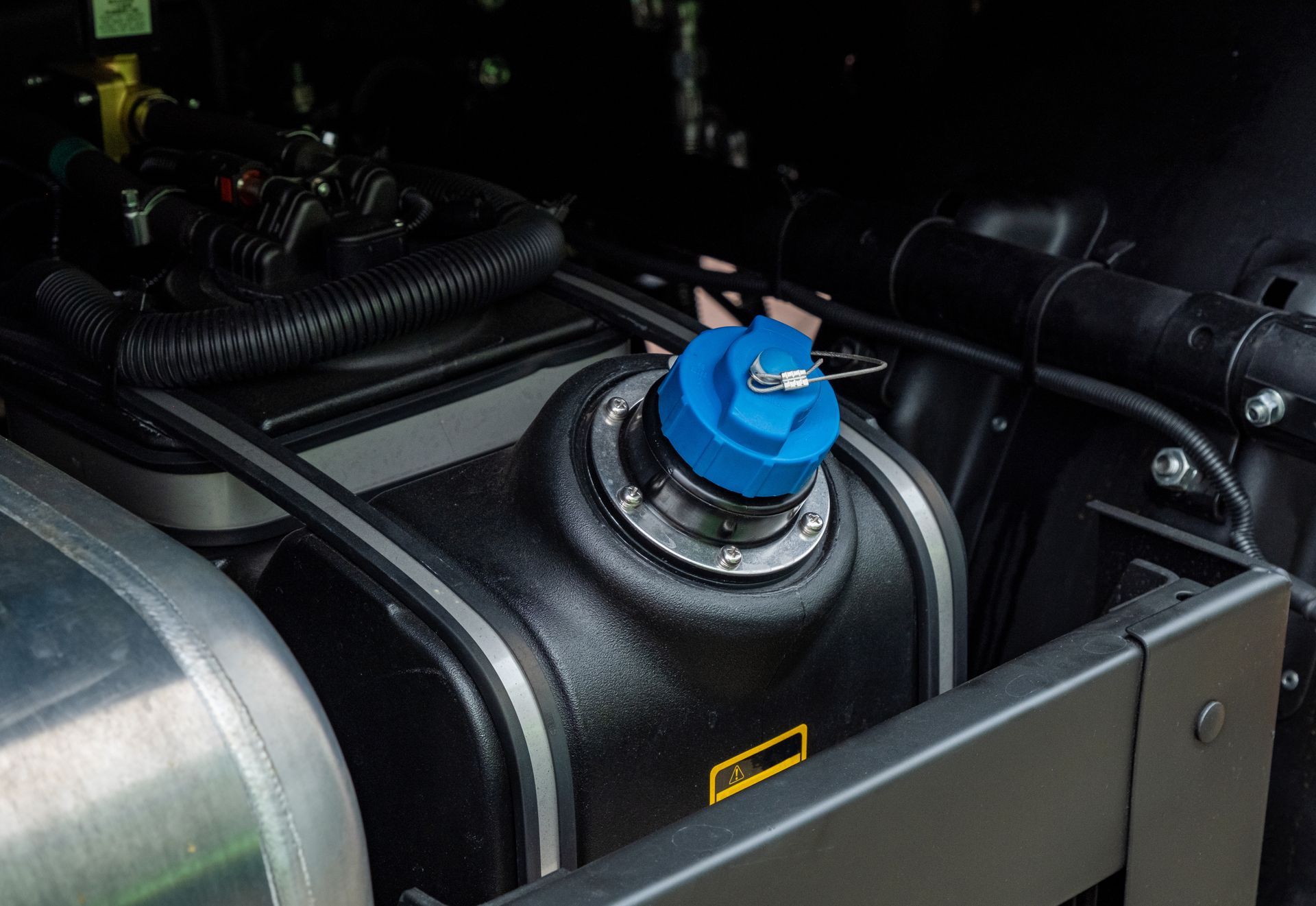 Blue cap on a black fluid reservoir in a vehicle's engine bay, likely for diesel exhaust fluid.