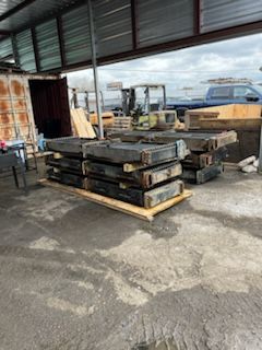 Pallet of rectangular metal pieces in a warehouse, with a forklift and other equipment visible in the background.