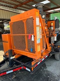 Orange industrial generator on a trailer, with a large metal grid in a shed-like structure.