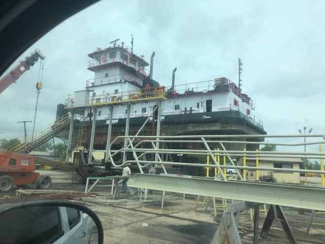 A large white and black tugboat on dry dock with workers and equipment on a cloudy day.