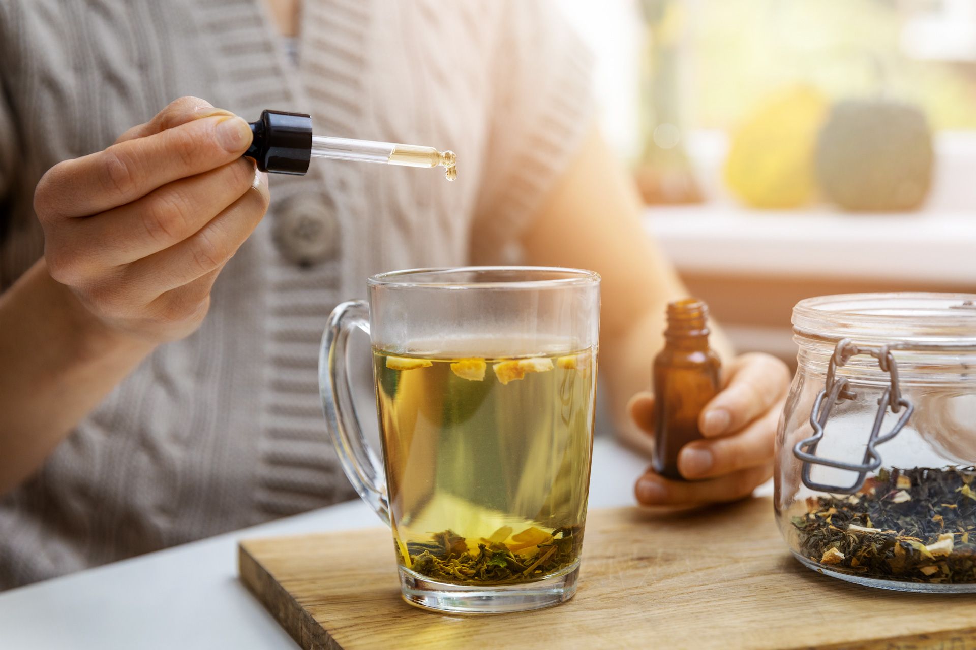 Woman adding drop of cbd oil in cup of tea with pipette for anti stress