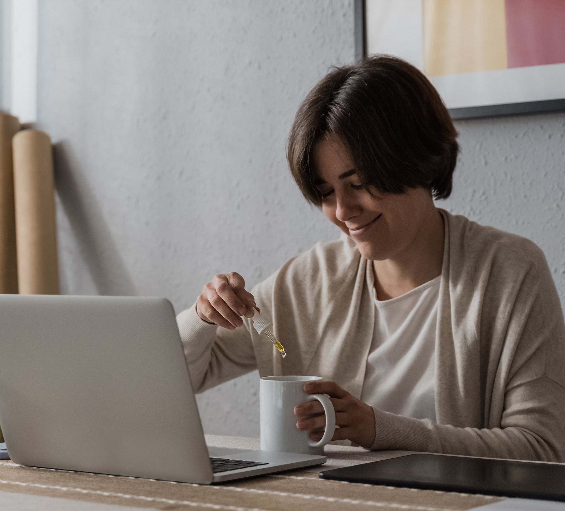Woman taking cannabidiol oil in tea cup while working at home office