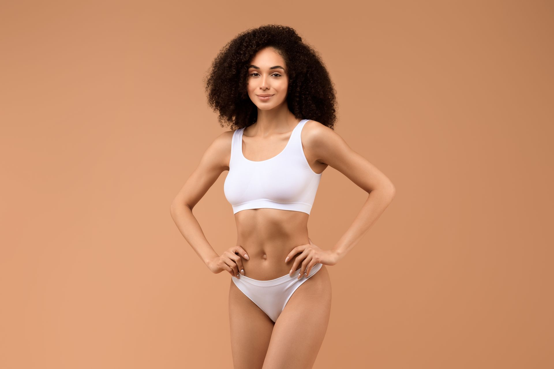 A woman in a white bra and underwear is standing with her hands on her hips.