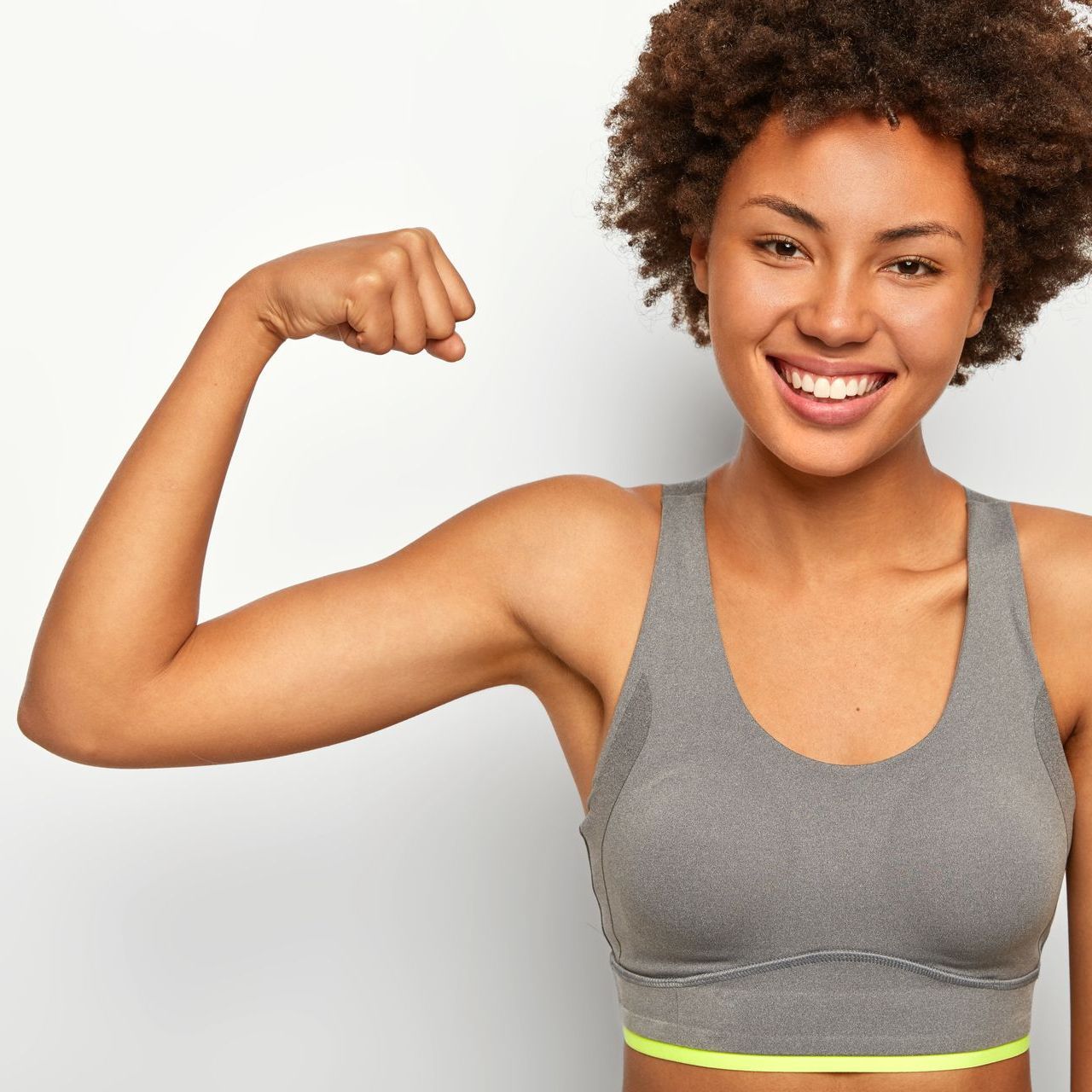 a woman in a gray sports bra is smiling and flexing her arm