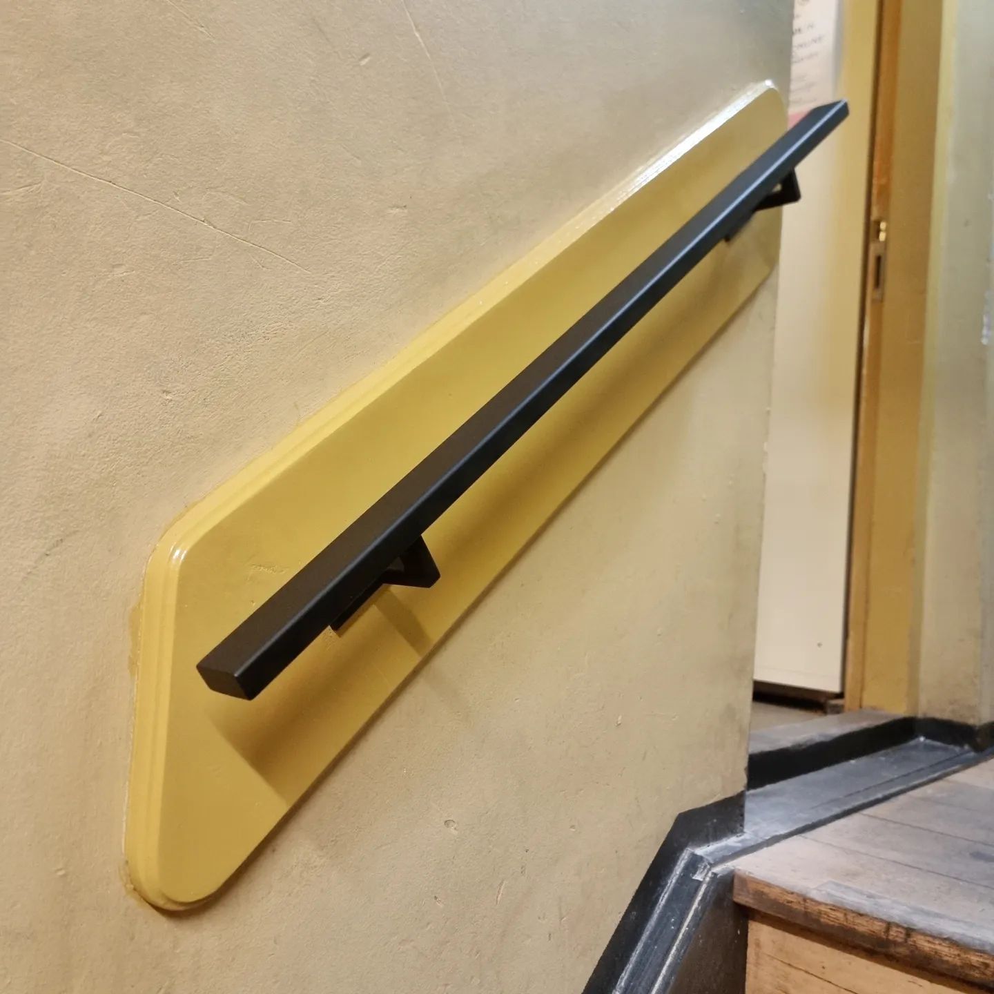 Een gele muur met een zwarte balustrade erop