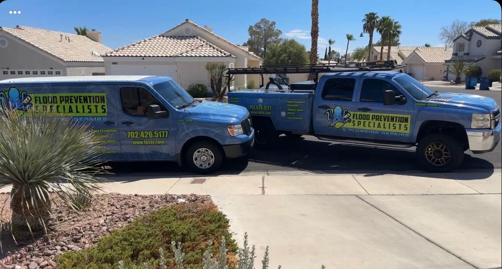 Two light blue service vehicles parked in front of houses; one a van and one a pickup truck, both with logos.