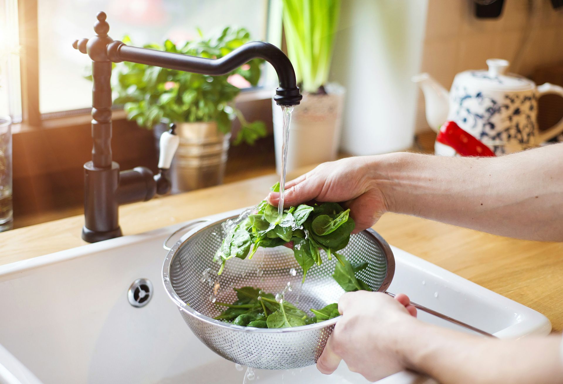 Person washing fresh spinach in a colander under a kitchen faucet.