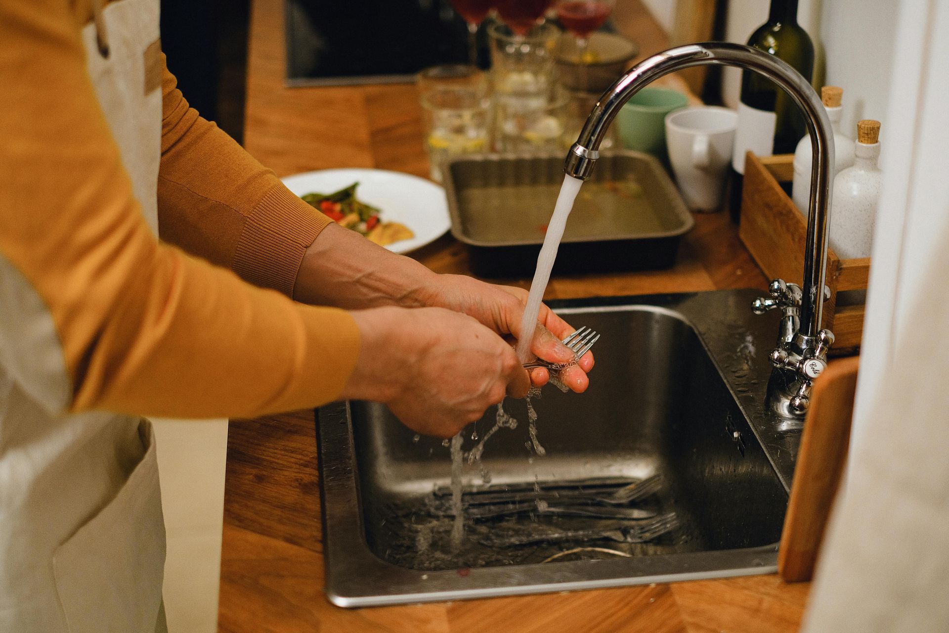 Person washes silverware in kitchen sink with water running.