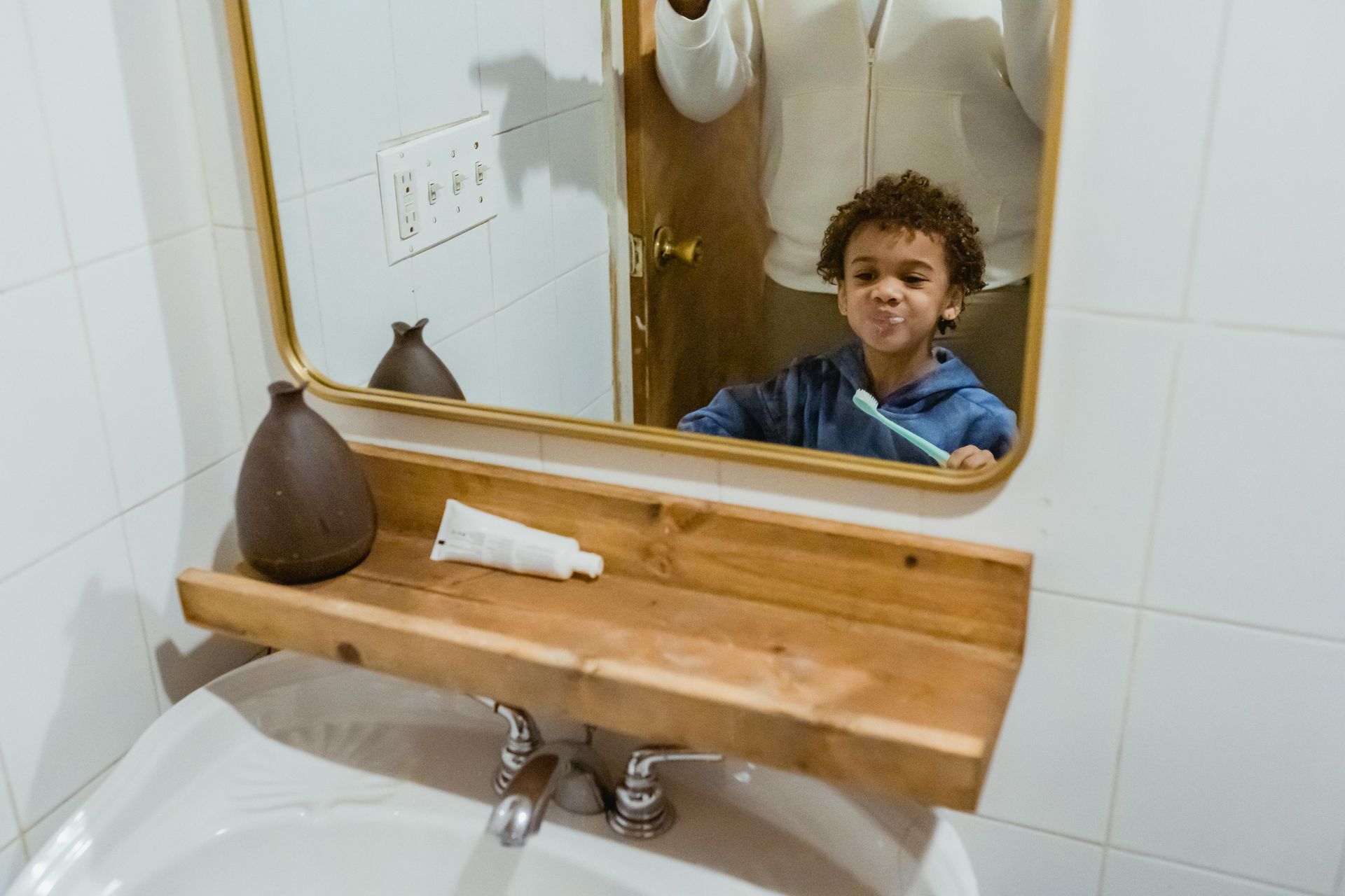 Boy brushing his teeth in the bathroom mirror, toothpaste and brush visible.