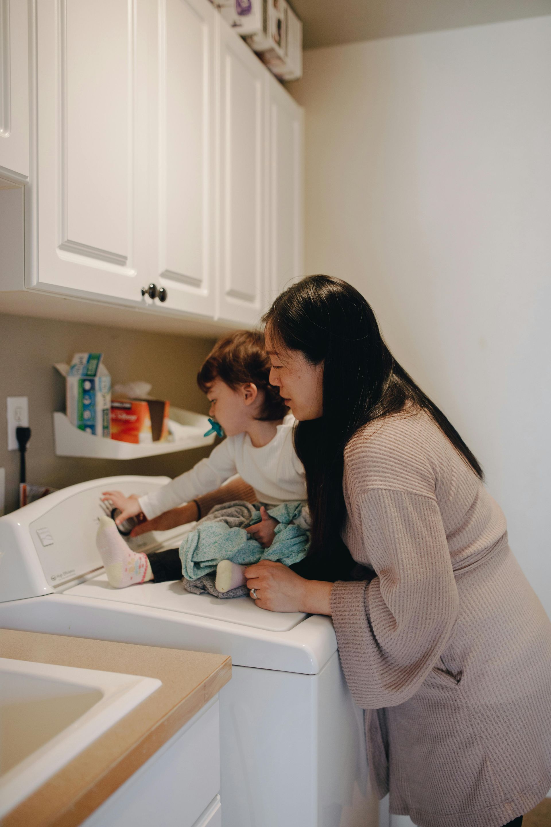 Woman and child in laundry room, looking at clothes on the washing machine.