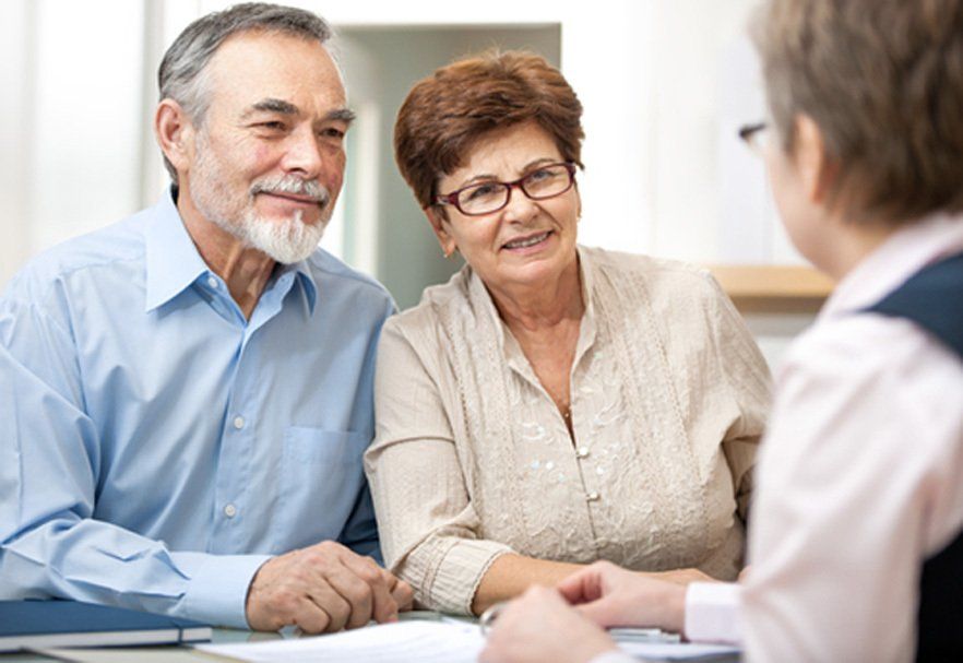 An elderly couple is sitting at a table talking to a woman.